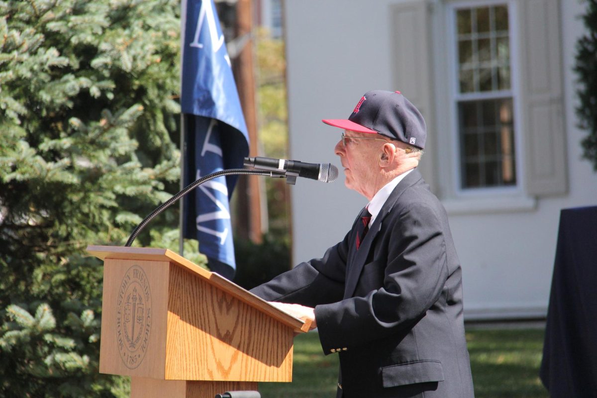 Paul Mecray addresses the students and adults in attendance, wearing an MFS baseball cap gifted to him the morning of the ceremony. Photo by Emmie Huynh ’27.
