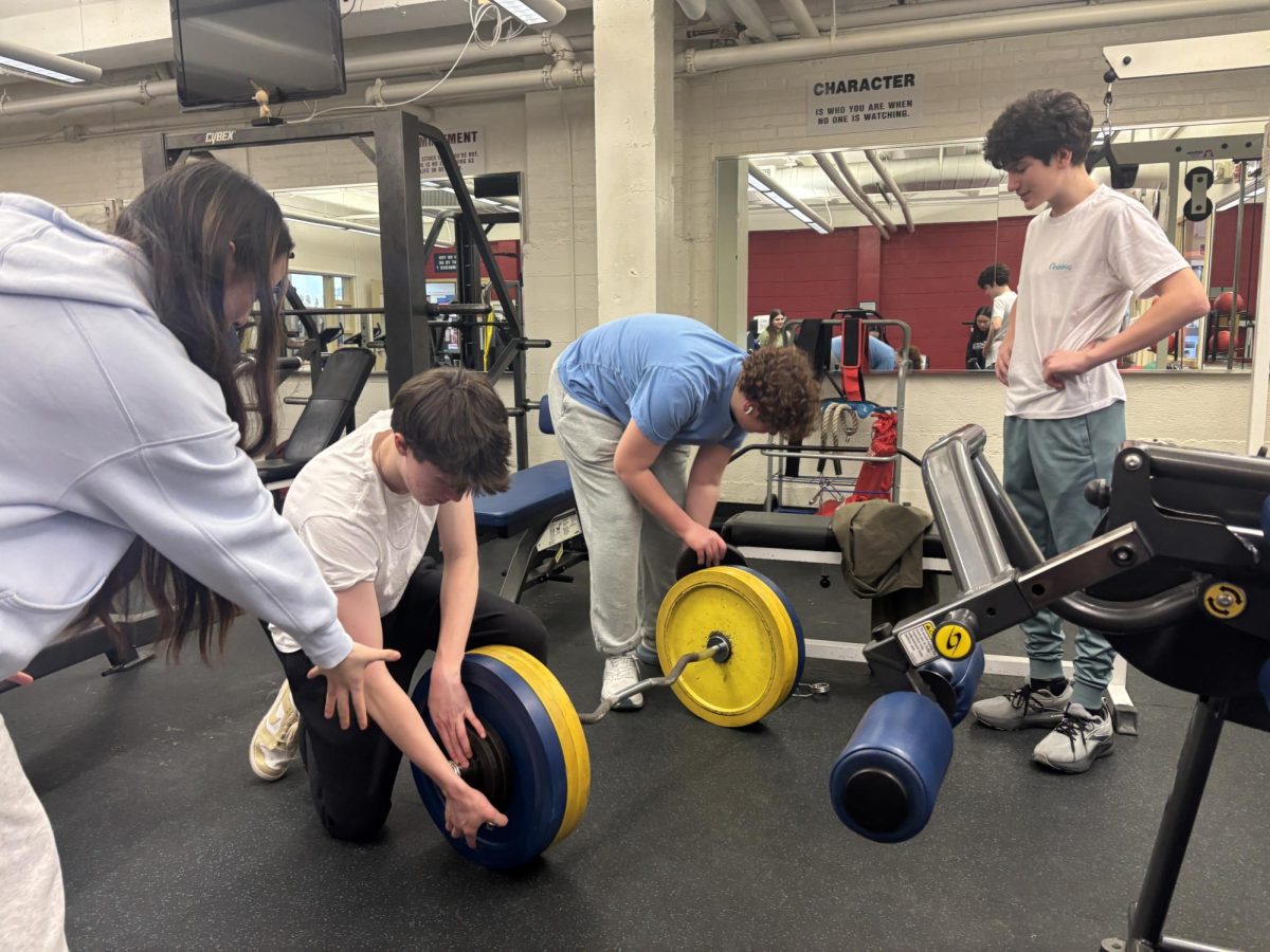 Students in the Weight Room work together to put weights onto a barbell. Photo by Emmie Huynh ’27.